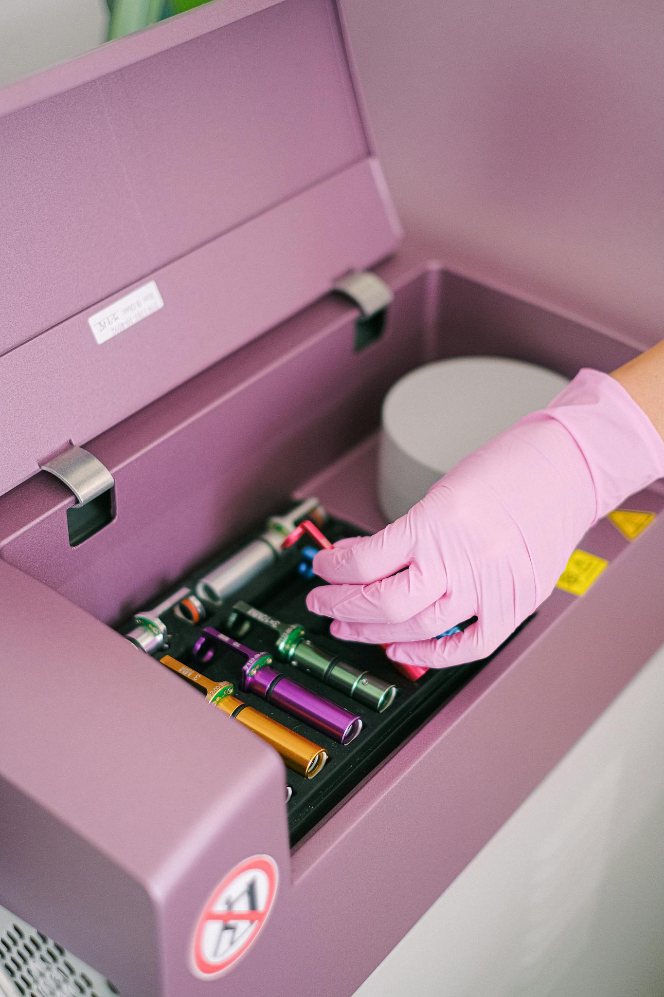 A hand in a pink glove handling ink cartridges inside pharmacy equipment, showcasing organized workspace.