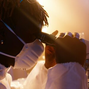Scientist wearing protective gear examining samples under a microscope in a laboratory.